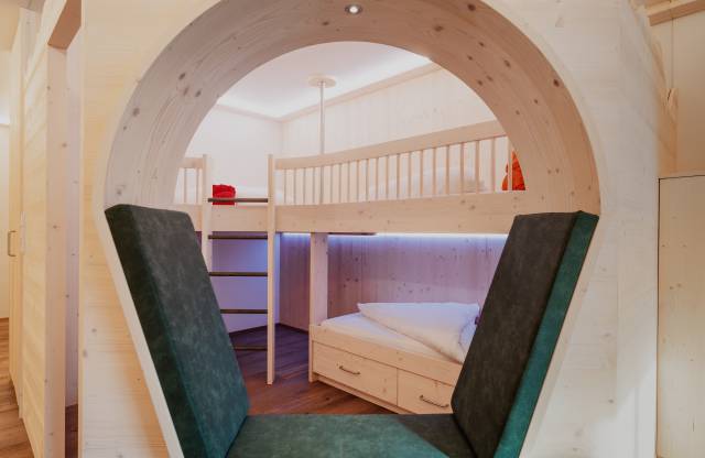 Helles Familienzimmer mit Stockbett und Sitzgelegenheit.