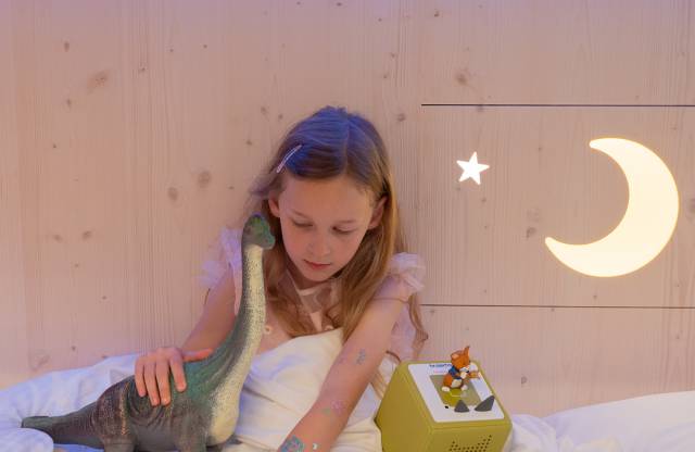 Child lying in bed with their toy at Tirolerhof.