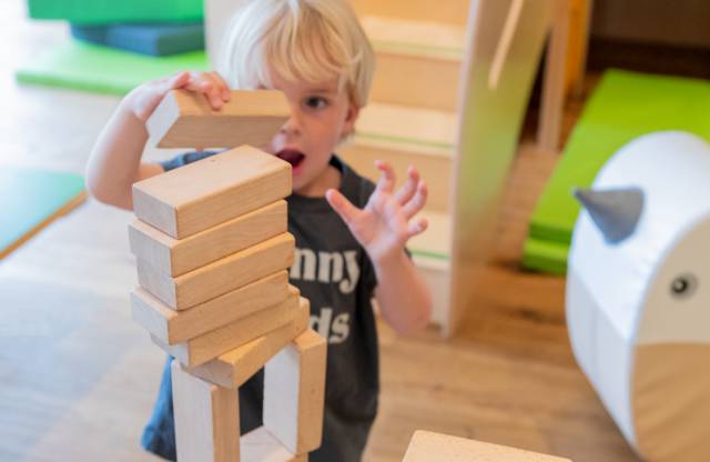 Kleinkind spielt mit Holzbausteinen im Kinderclub im Tirolerhof.