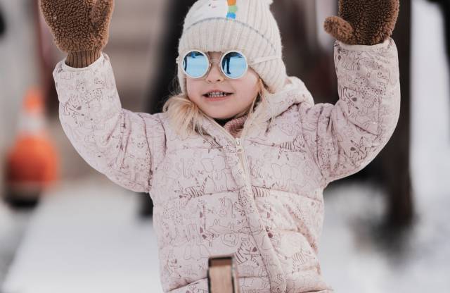 Kleines Kind sitzt warm eingepackt auf dem Rodel im Schnee.