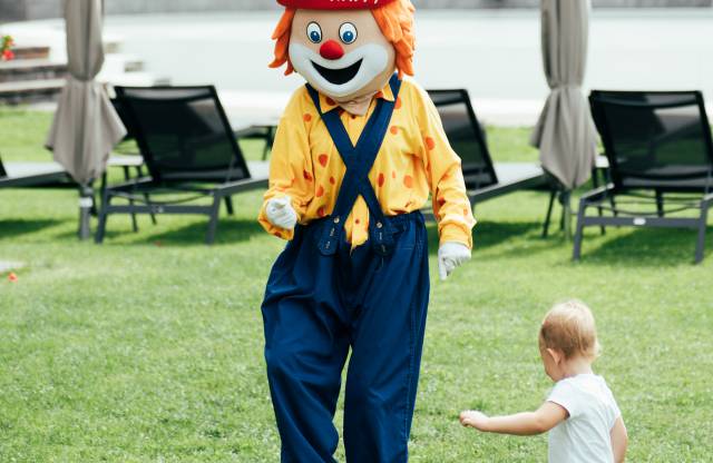 Familotel Maskottchen Happy spielt mit einem Kind Fußball im Garten des Familienhotels Tirolerhof.