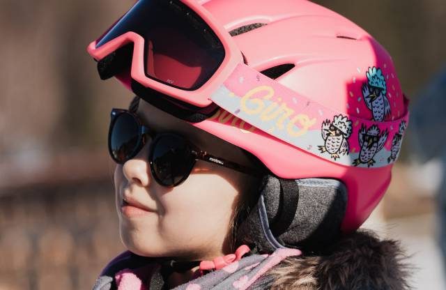Mädchen mit pinkem Skihelm und Sonnenbrille.
