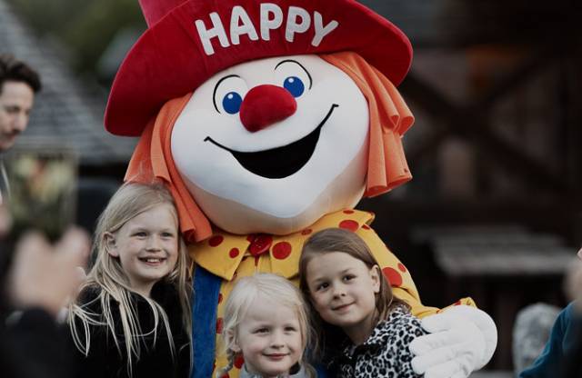Familotel Happy hält drei Kinder im Arm, die in die Kamera lächeln.