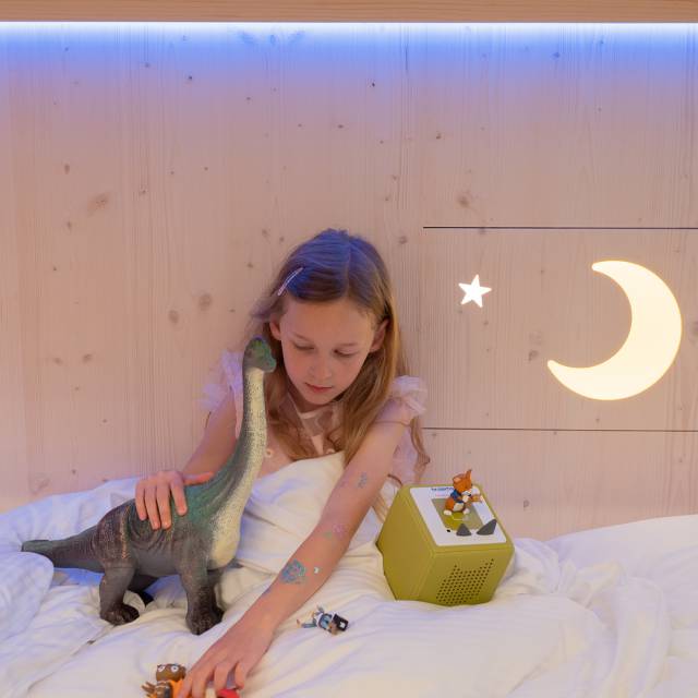 Child lying in bed with their toy at Tirolerhof.