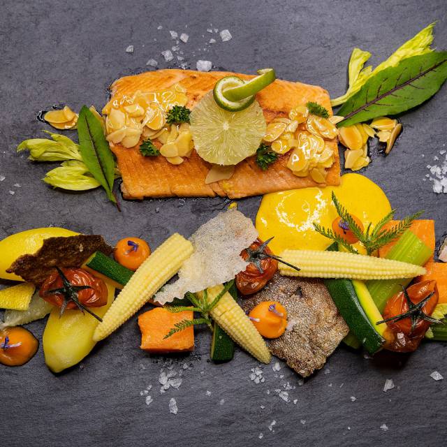 Gebratener Lachs mit frischem Gemüse kunstvoll angerichtet auf einer Schieferplatte im Tirolerhof.