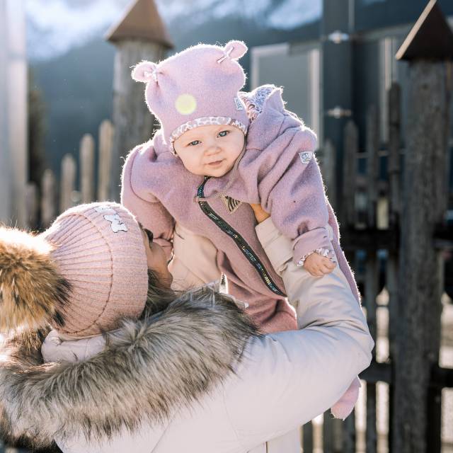Mutter hält Baby in rosa Winterkleidung in die Höhe.
