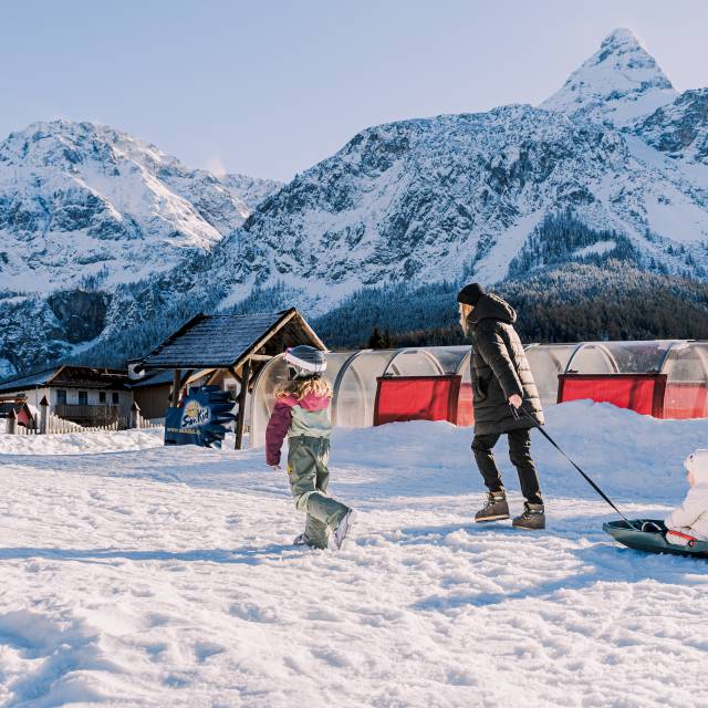 Mutter zieht Kinder auf dem Schlitten durch den Schnee.