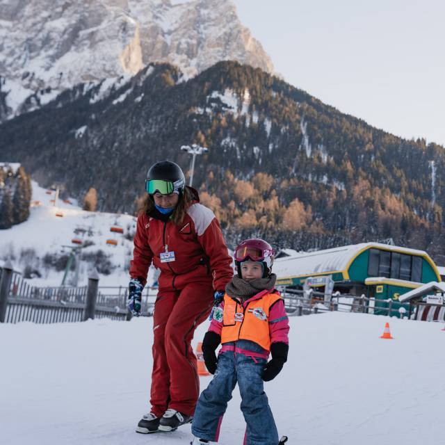 Kind mit Skilehrerin vor einem Skilift beim Ski fahren lernen.