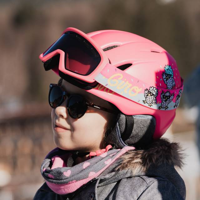 Mädchen mit pinkem Skihelm und Sonnenbrille.