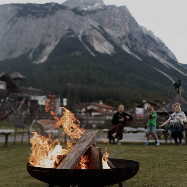 Familie sitzt an einem Lagerfeuer, umgeben von Bergen.