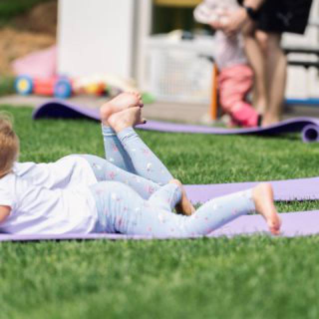 Spielerische Yoga-Übungen mit Kindern auf einer Wiese.