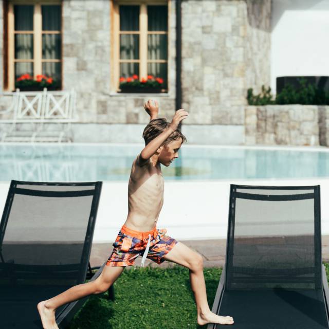 A boy in swim trunks running around the outdoor pool at Tirolerhof.
