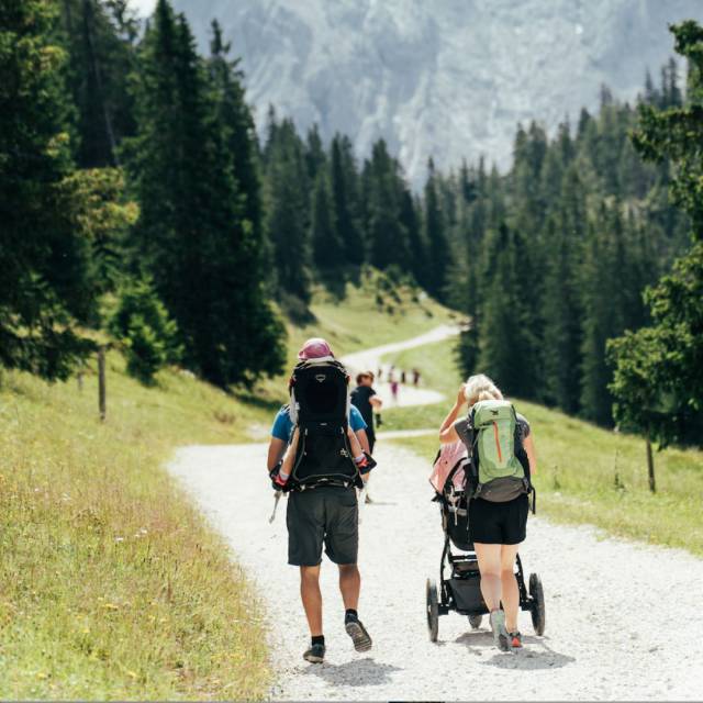 Familie mit Kinderwagen und Rucksack auf einer familienfreundlichen Wanderung.