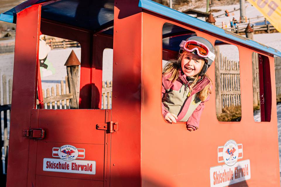 Kind schaut aus einem roten Fahrzeug der Skischule Ehrwald raus.