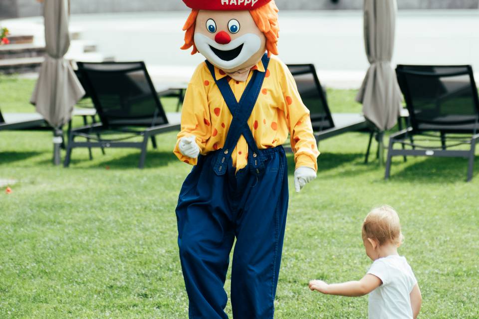Familotel Maskottchen Happy spielt mit einem Kind Fußball im Garten des Familienhotels Tirolerhof.