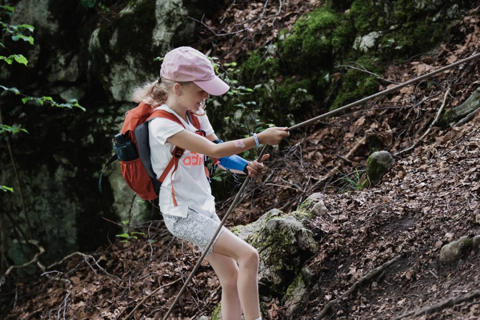 Mädchen wandert im Wald und hält sich an einem Seil fest.