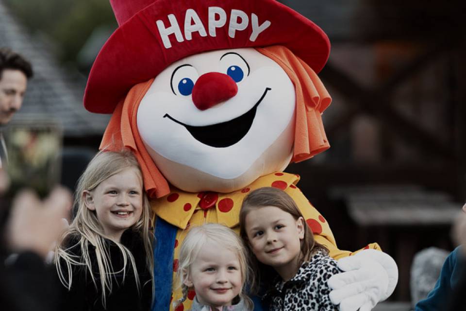 Familotel Happy hält drei Kinder im Arm, die in die Kamera lächeln.