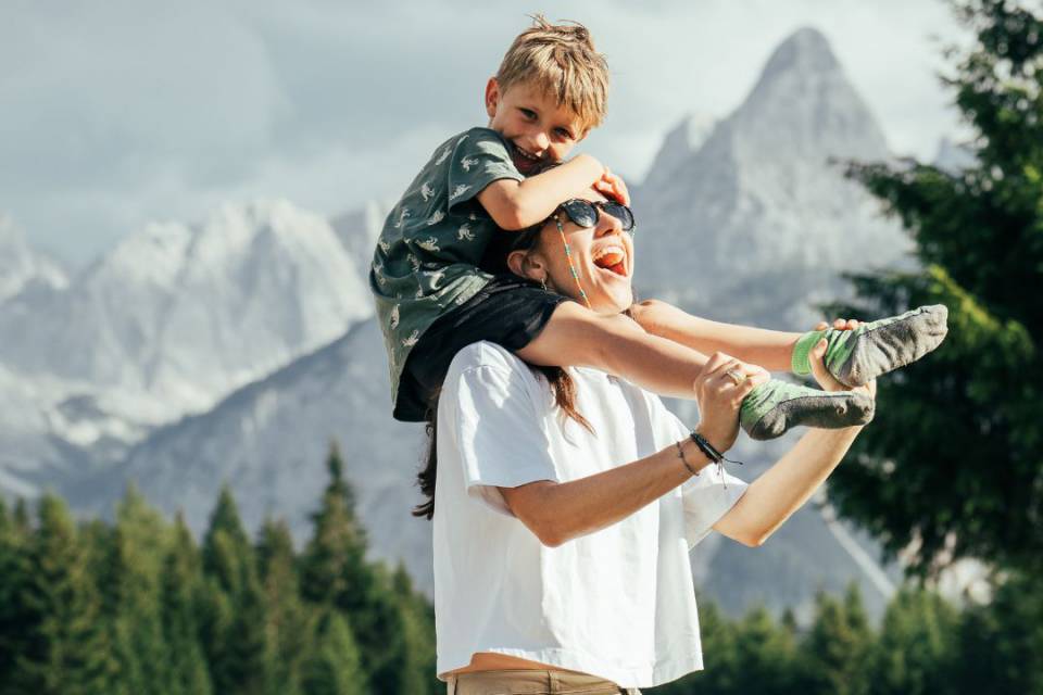 Mama trägt ihr Kind auf den Schultern bei einer Familienwanderung in den Tiroler Bergen.