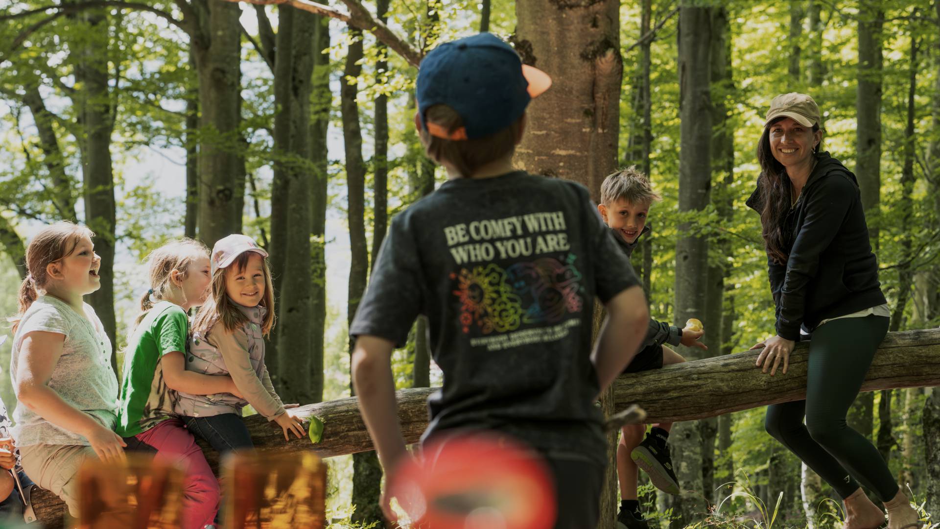 Kinder spielen gemeinsam im Wald auf einem Holzstamm.