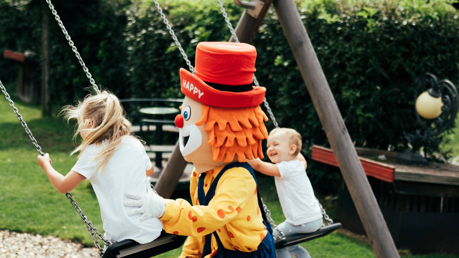 Familotel Maskottchen Happy spielt mit zwei Kindern auf dem Spielplatz des Tirolerhofs.