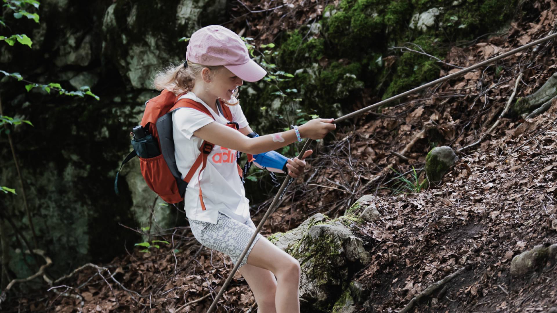 Mädchen wandert im Wald und hält sich an einem Seil fest.