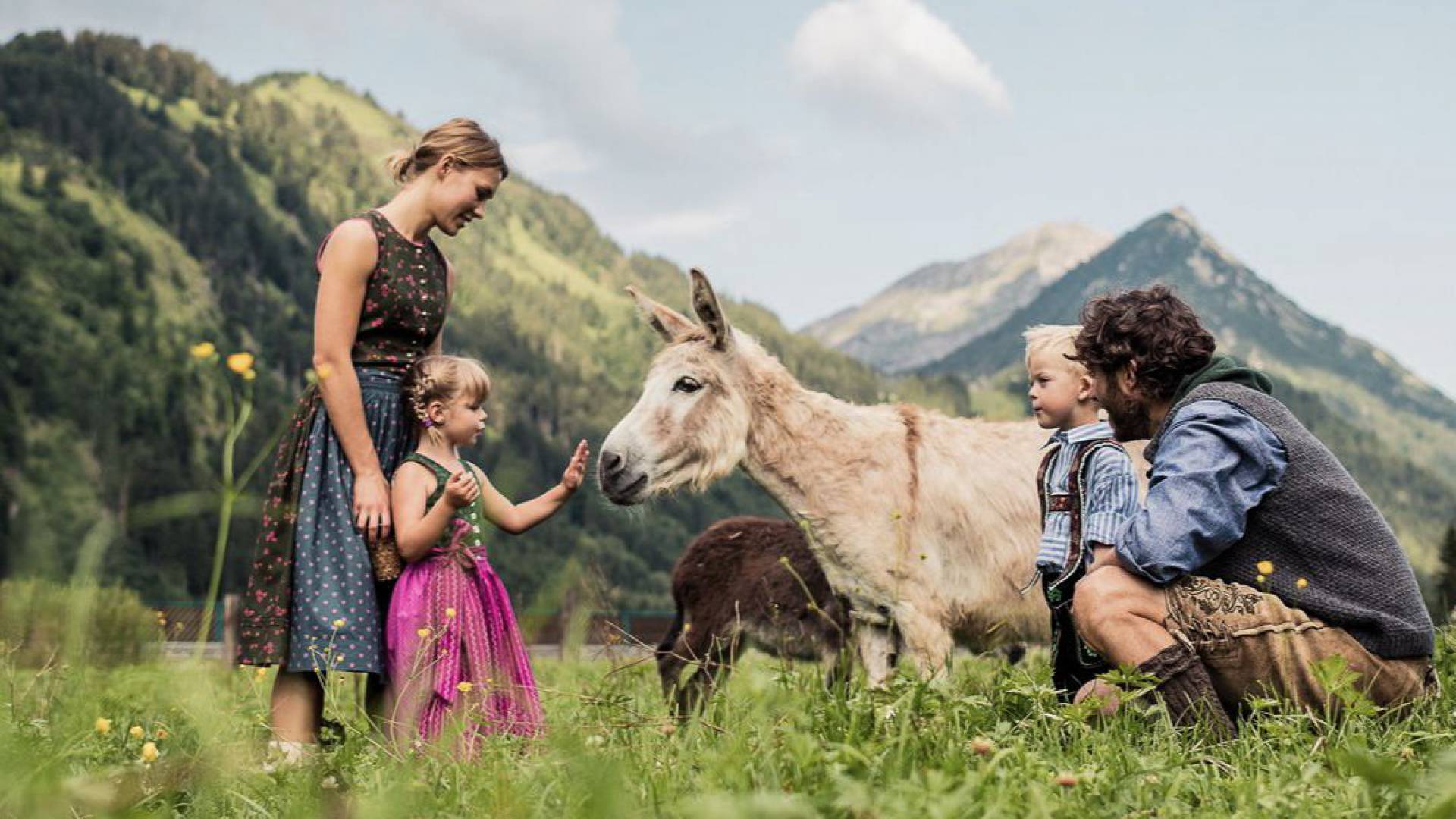 Eine Familie in Tracht steht auf einer Wiese und streichelt einen Esel.