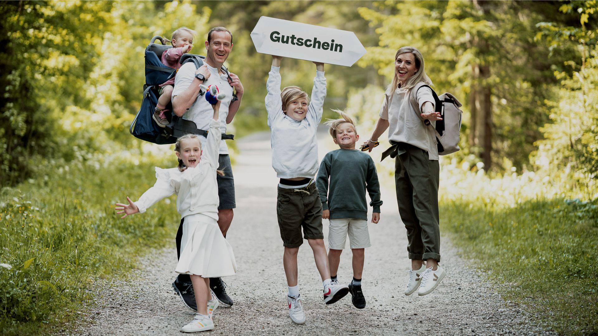 Fröhliche Familie die im Wald stehen und ein Schild hochhalten.